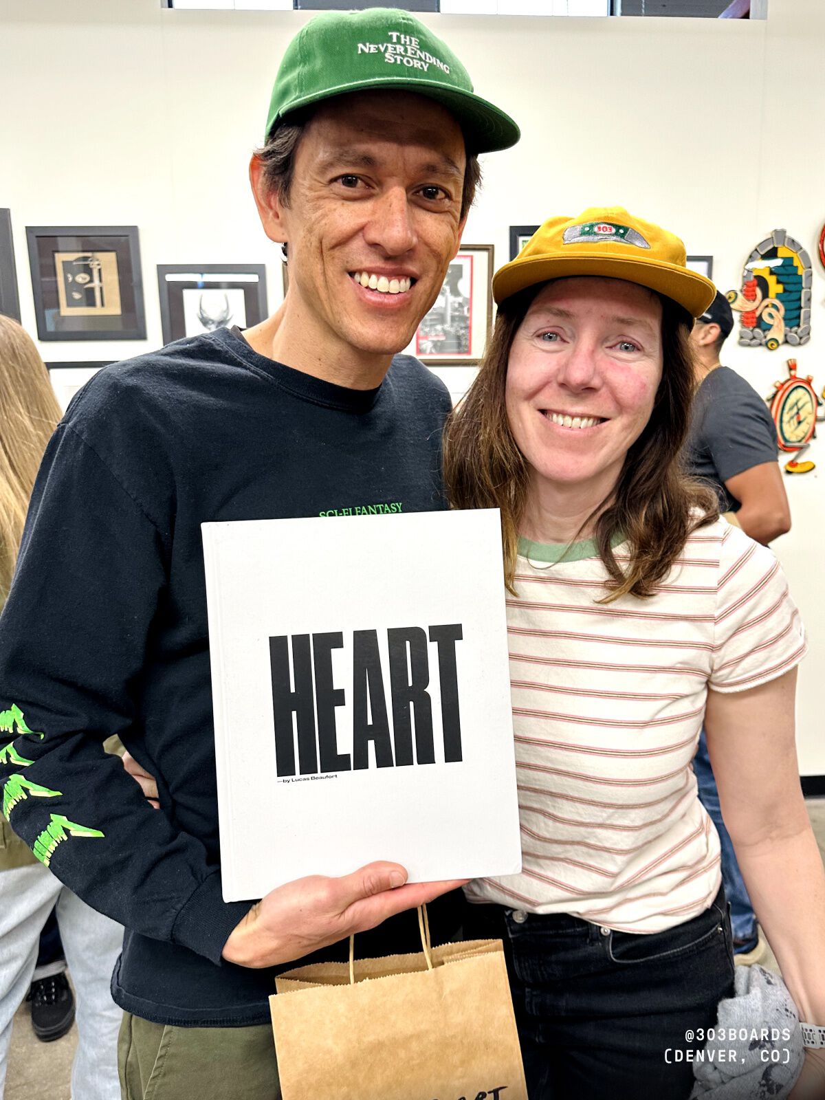 Photo of two people holding a white sign with black text reading heart.